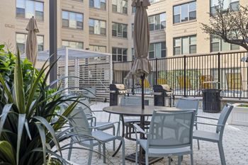 A patio with grey chairs and tables is surrounded by a black fence.